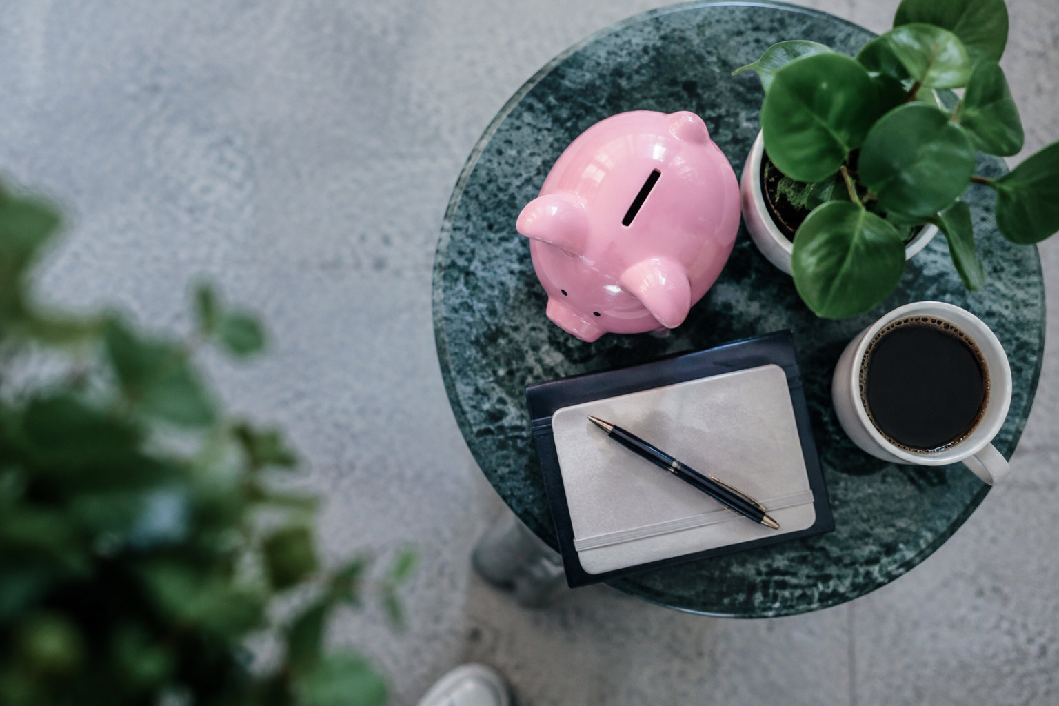 Tirelire rose, carnet, stylo et plante sur une table ronde en marbre vert, vue de dessus.